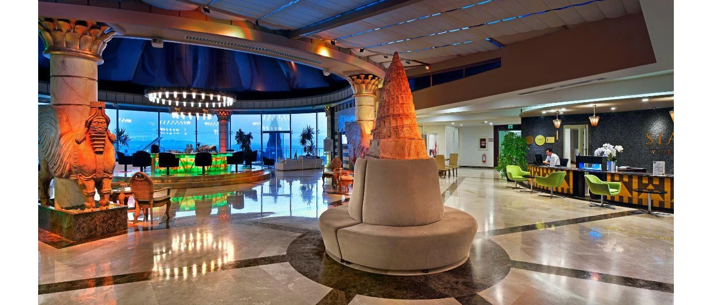 Lobby with marble floor, circular seating, columns with statue designs, and a desk with green chairs