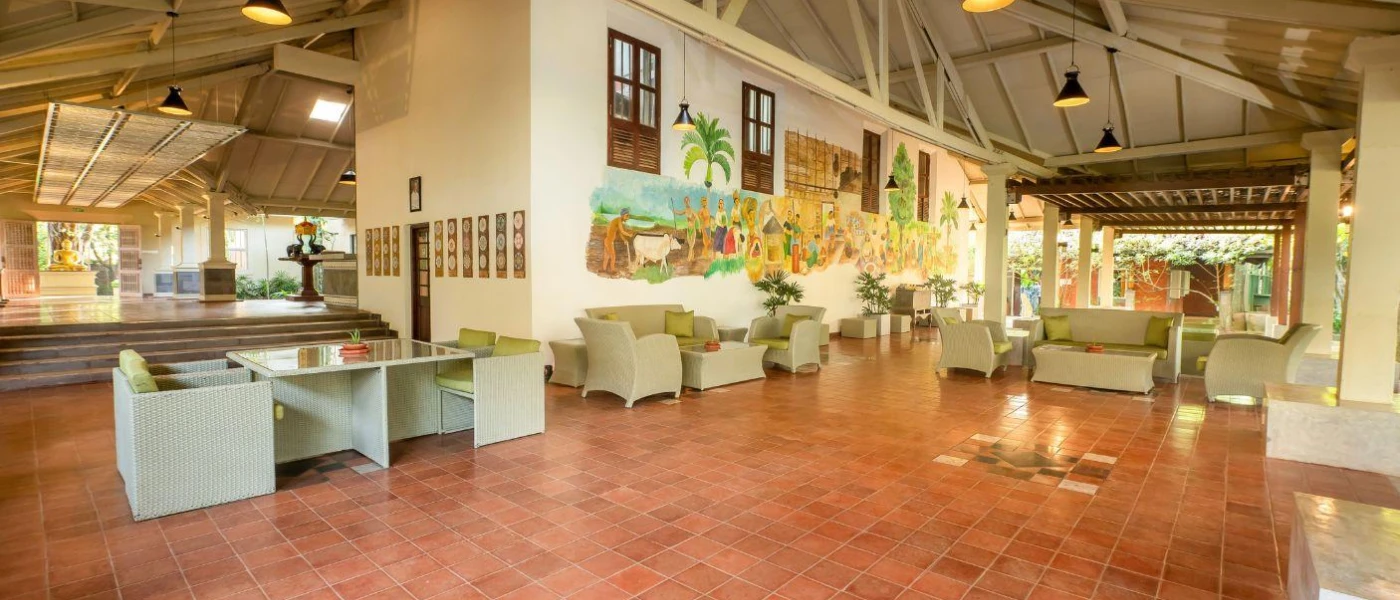 Airy reception area with terracotta tiled flooring, white walls, grey rattan furniture and a colourful wall mural depicting local Sri Lankan life