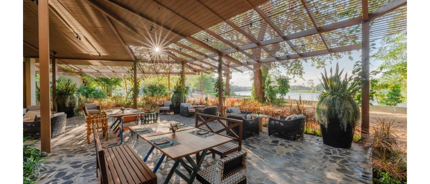 Open-sided outdoor dining area, with a stone floor, wooden tables and chairs and a view of the lake and gardens