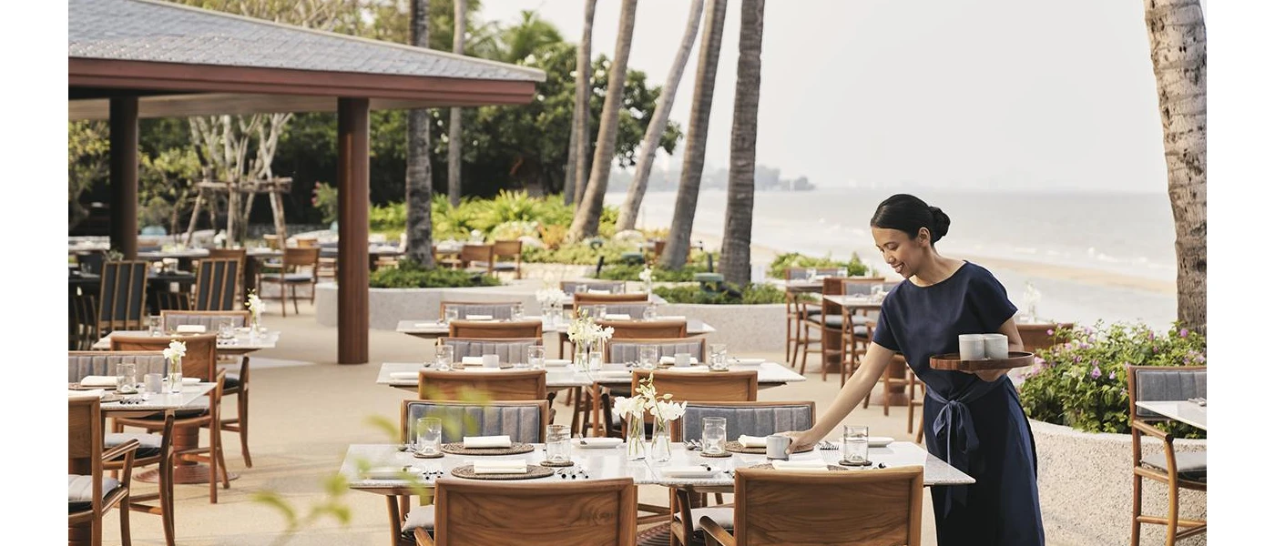 Woman sets tables an a beachfront terrace with the ocean in the background