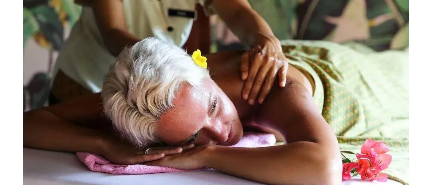 Woman lies on her back with a yellow flower in her hair, relaxing as a therapist massages her back