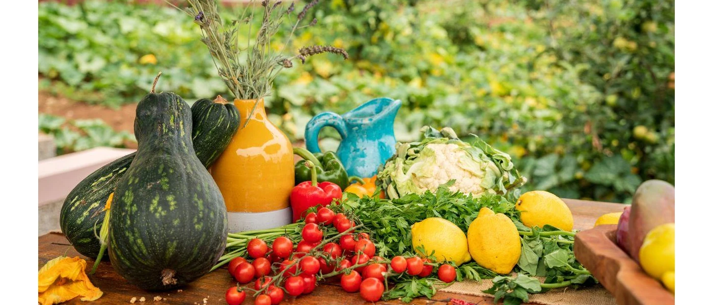 Ceramic jugs next to lemons, vine tomatoes and squash in an outdoor setting