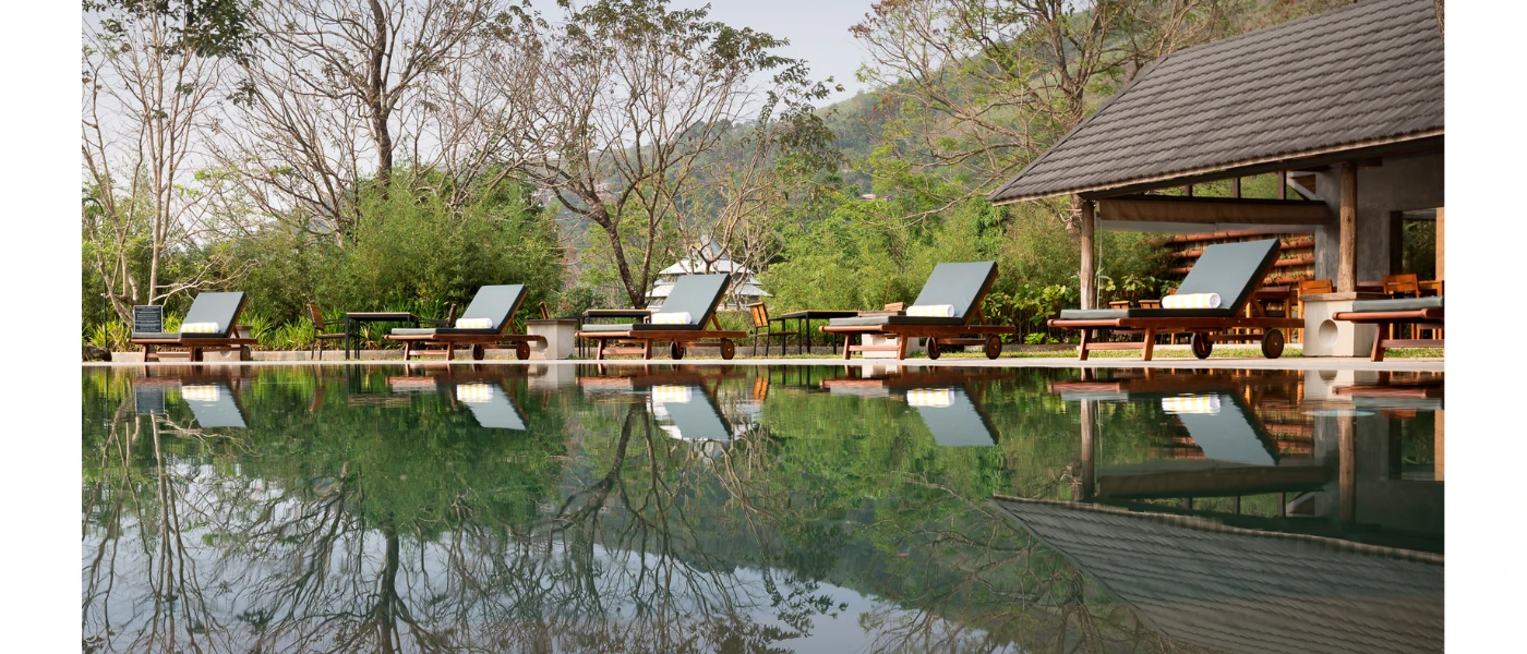 Swimming pool lined with white loungers and surrounded by greenery