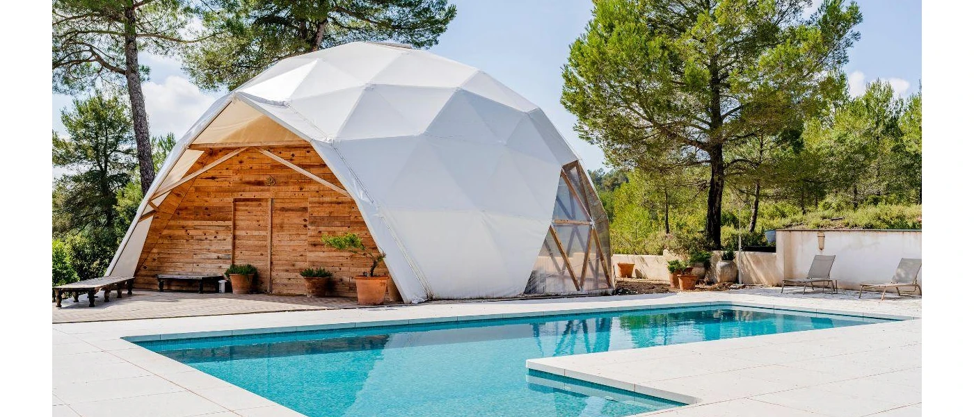 Wooden dome with a white cover next to a swimming pool among gardens