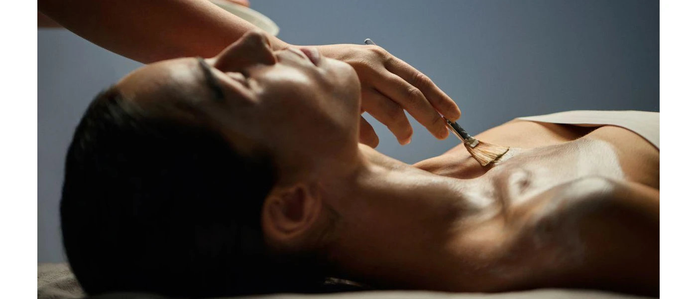 Woman lies on her back with her eyes closed as a therapist uses a brush to apply 