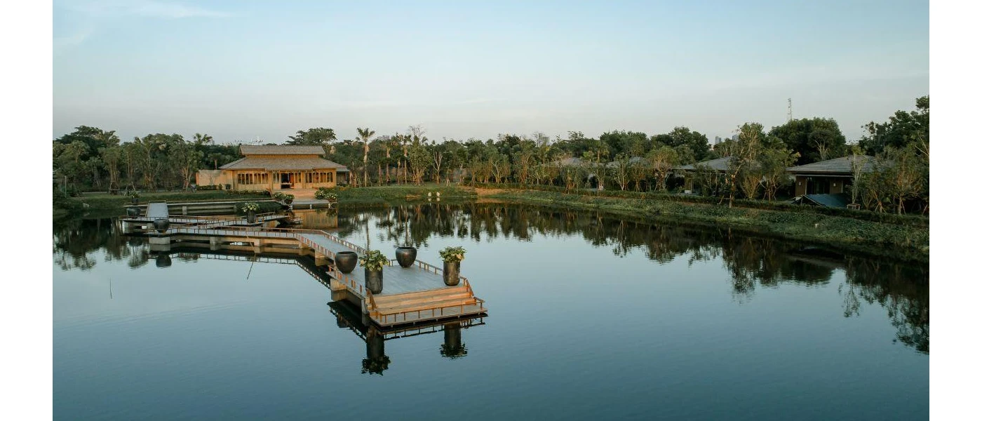 Wooden building with a grey-tiled roof, overlooking a river and wooden jetty and surrounded by greenery