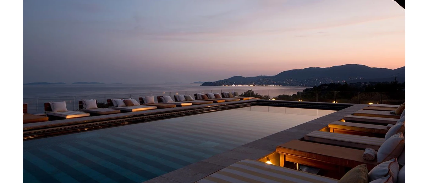 Twilight by a sea-facing pool, with chic striped daybeds, in-wall lighting and a view of the mountains in the background