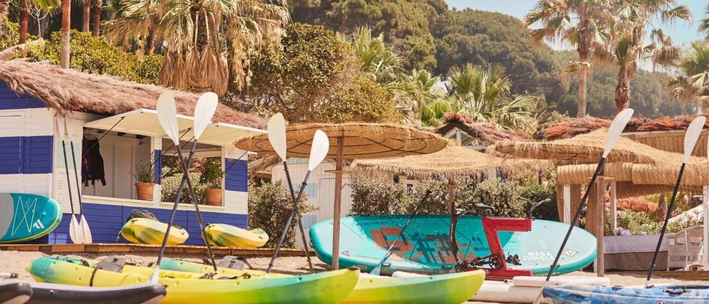 Thatched watersports hut with multi-coloured kayaks on the sand under thatched parasols