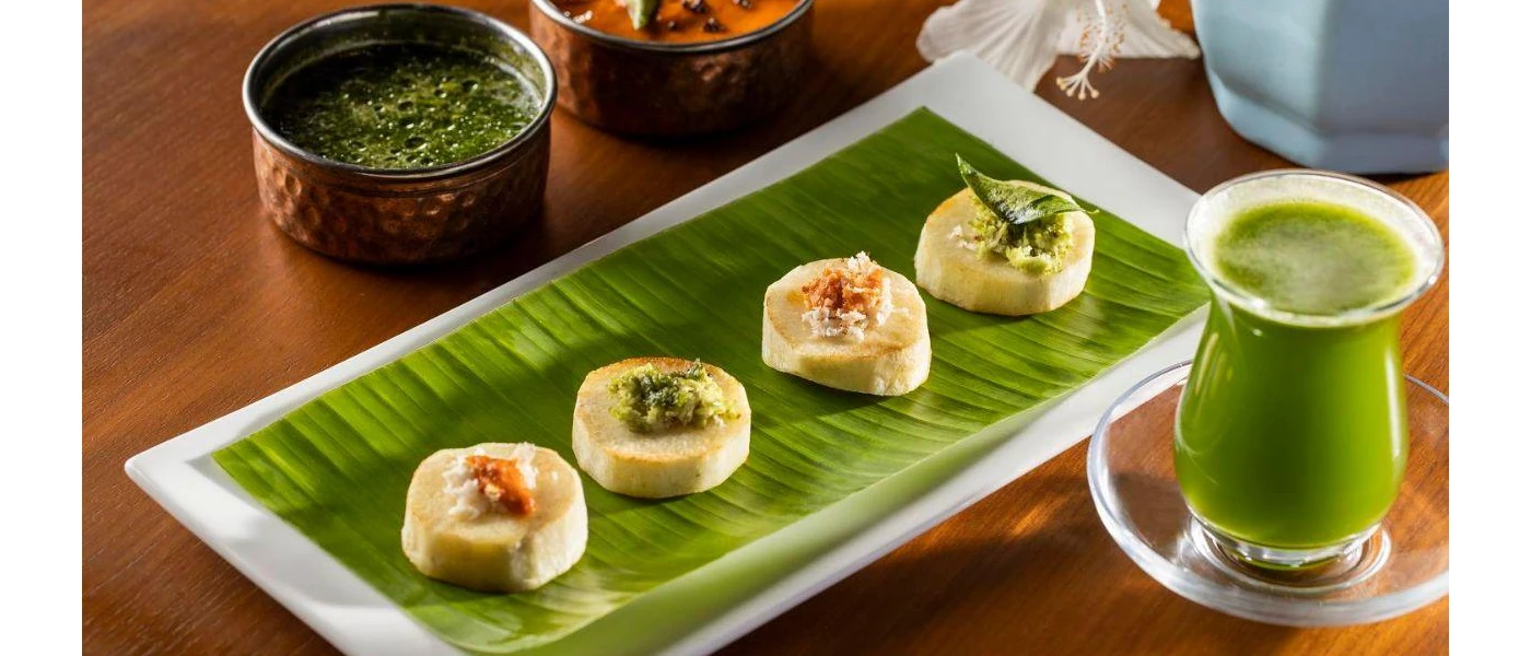 White plate topped with a green leaf and crostini with various toppings, next to a glass of green liquid