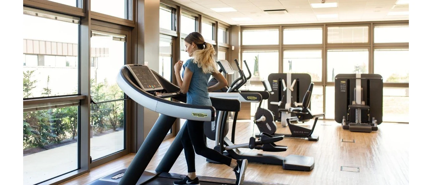 Woman in Nike trainers and a grey t shirt running on a treadmill in a bright gym with full-length windows
