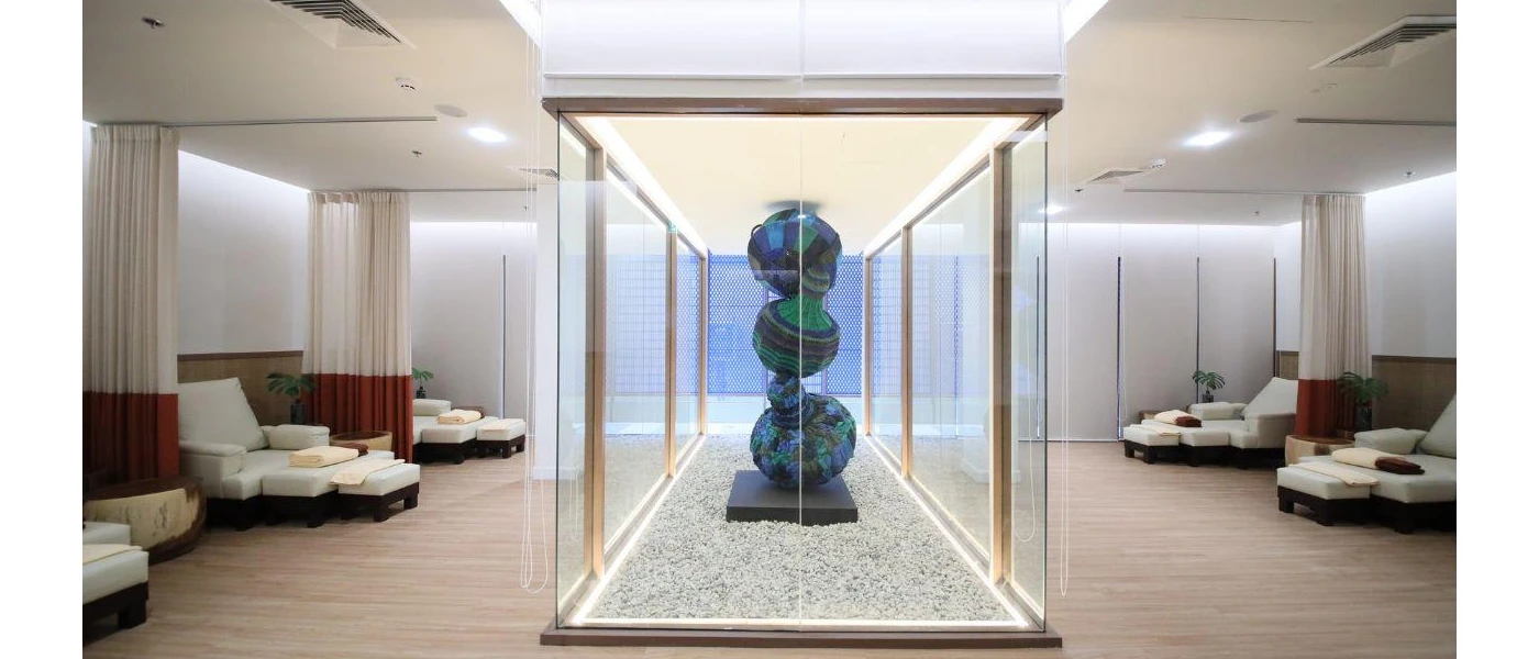 Glass case with a contemporary sculpture shaped like three stacked balls, surrounded by white-cushioned daybeds