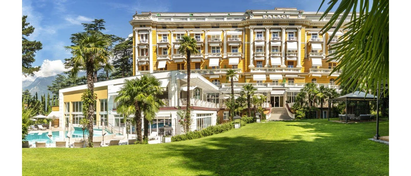 Landscaped gardens, a swimming pool surrounded by palms, and the exterior of Palace Merano