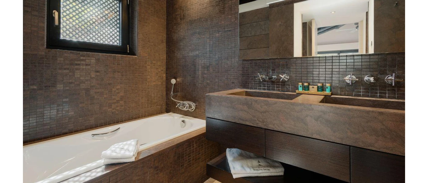 Brown marble bathroom with mosaic tiles, a large mirror and vanity unit and white bath