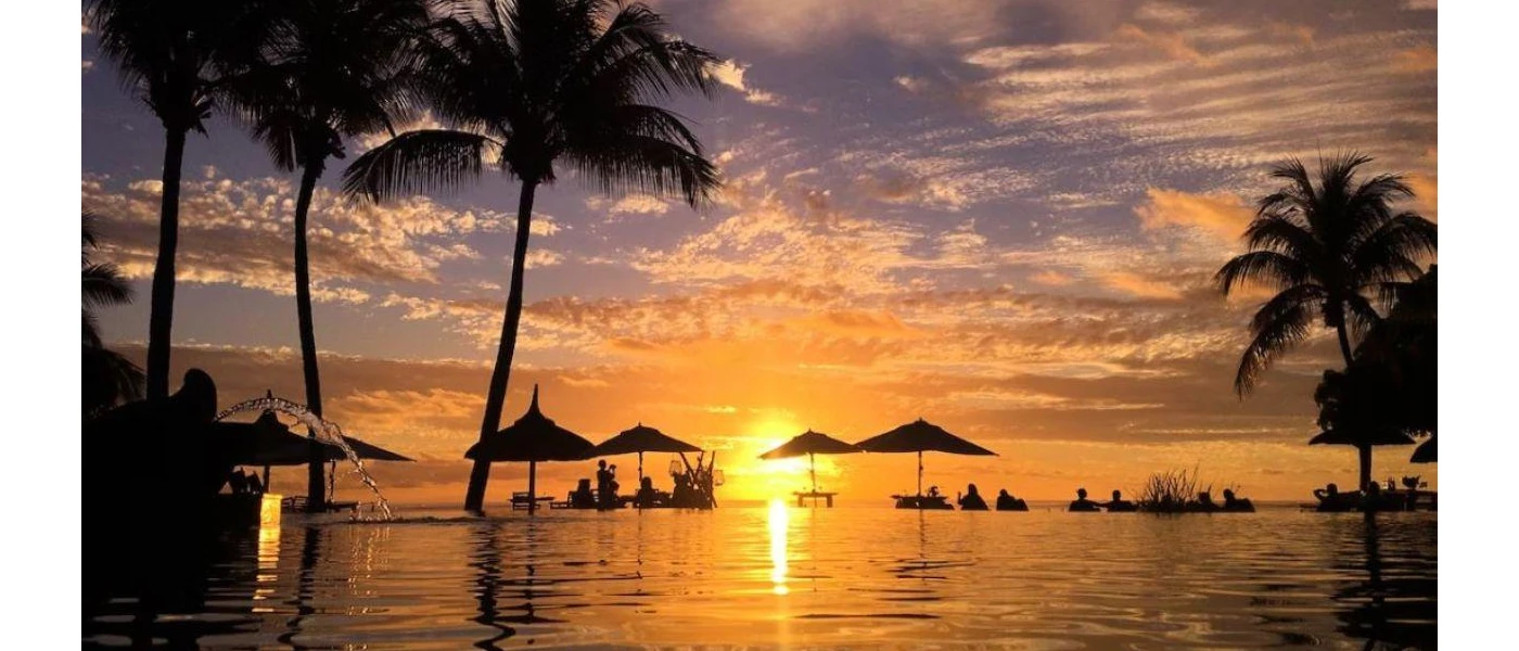 Ocean at sunset with palm trees and thatched umbrellas