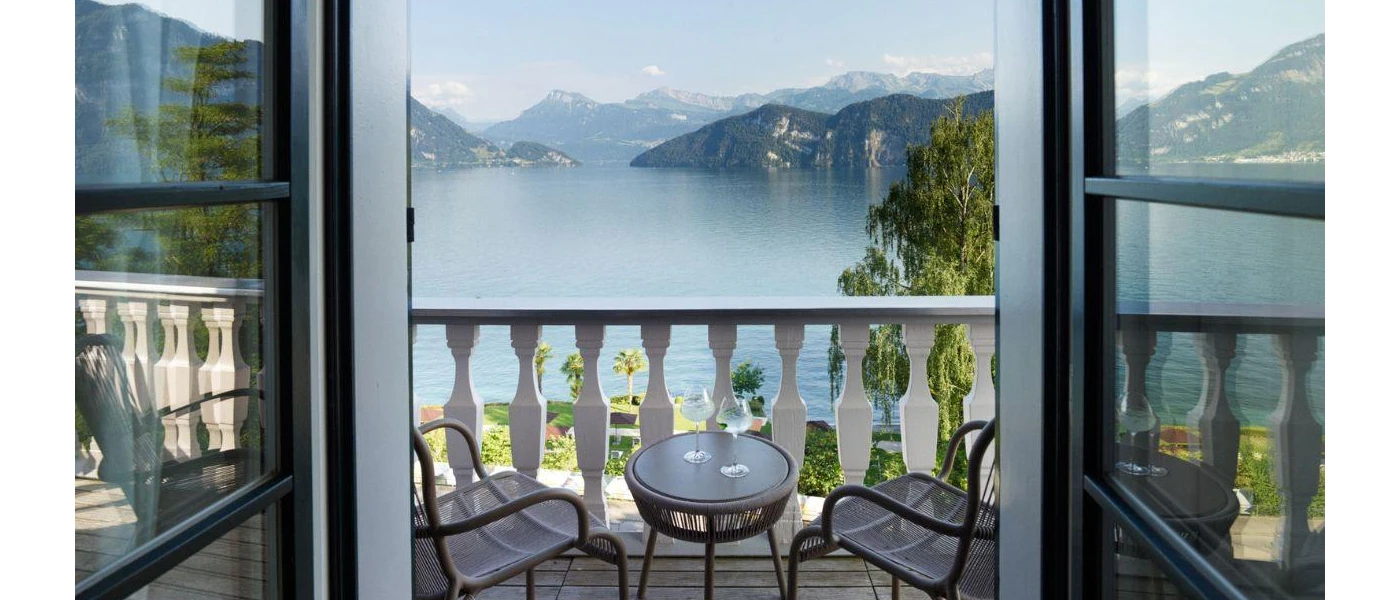 Balcony with white balustrades, a table and chairs and a view of a lake framed by mountains