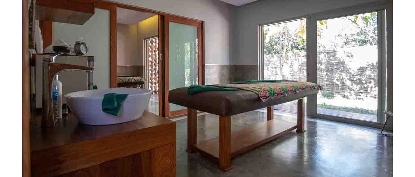 Treatment room with massage bed and white sink with a large window overlooking tropical greenery