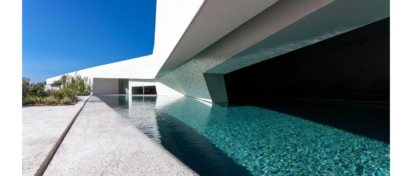 Wedge-shaped swimming pool next to an angular white building with a large dark window