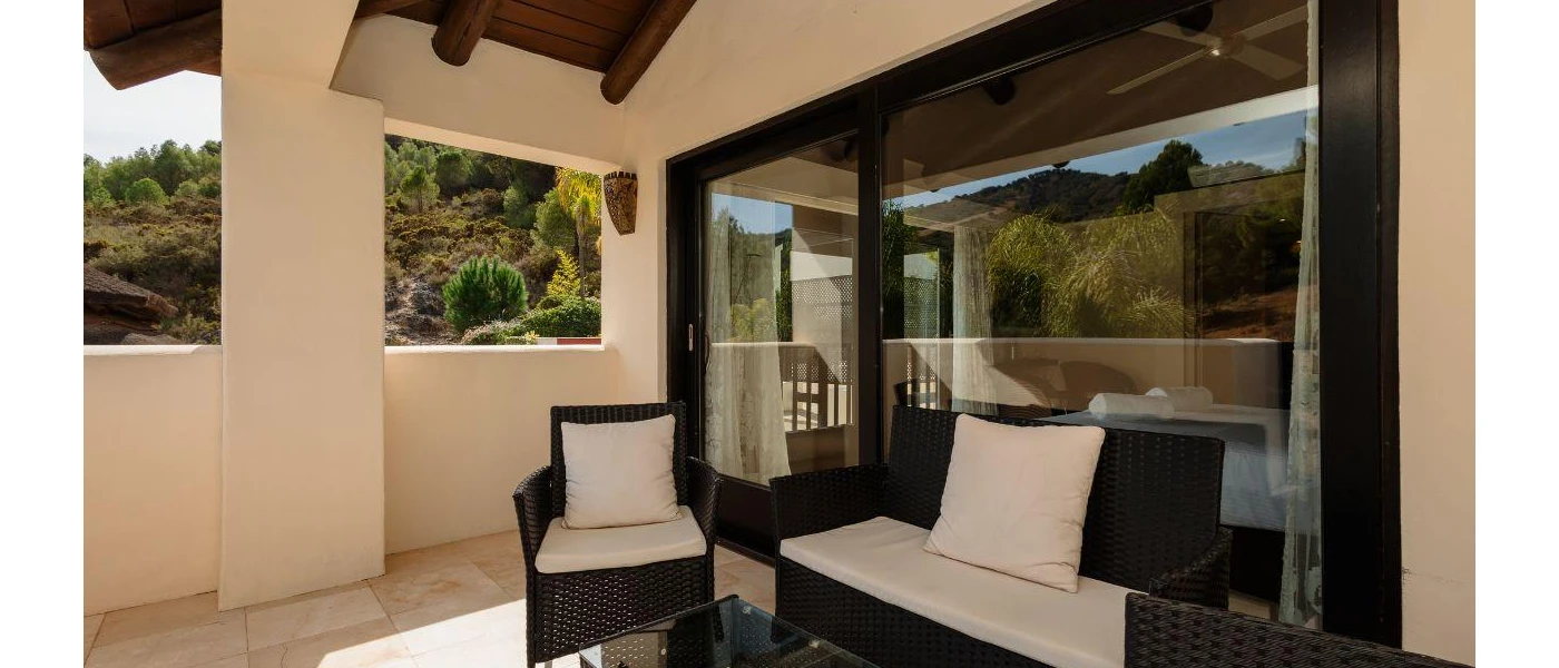 White concrete-walled terrace with black rattan chairs and white cushions