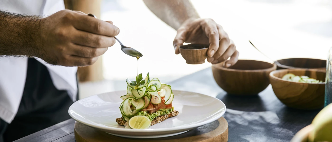 Chef drizzles dressing over a beautiful stacked salad dish, topped with cucumber