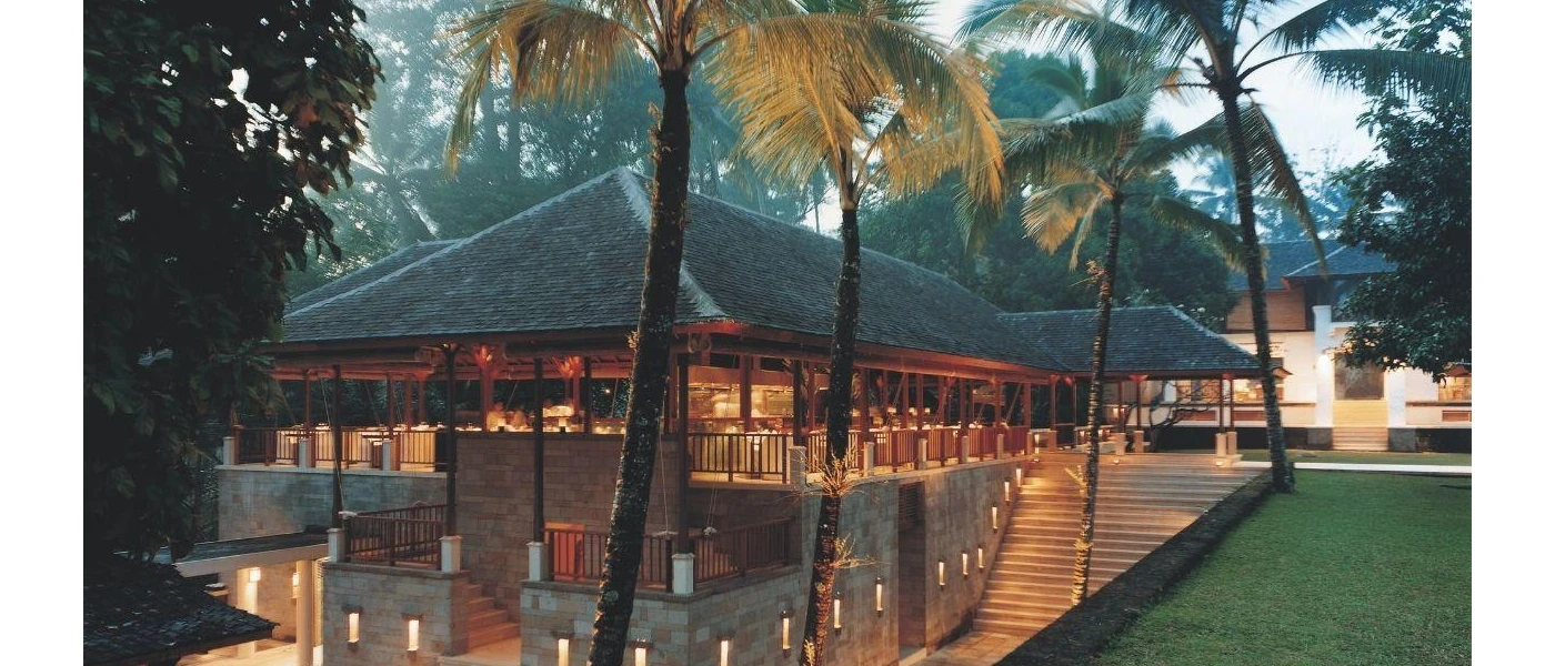 Tiled-roof buildings next to steps and a grass lawn, lit by lights as the sky darkens