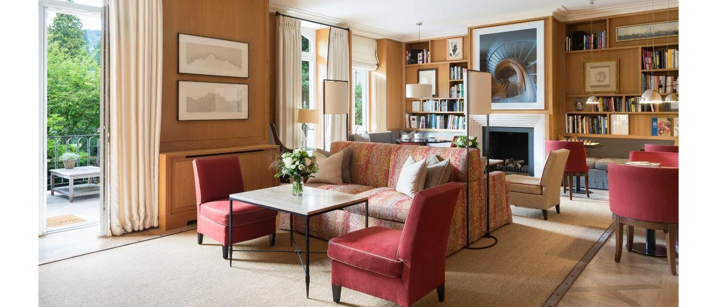 Lounge area with red velvet chairs and wood-panelled walls, bookshelves full of books and a fireplace