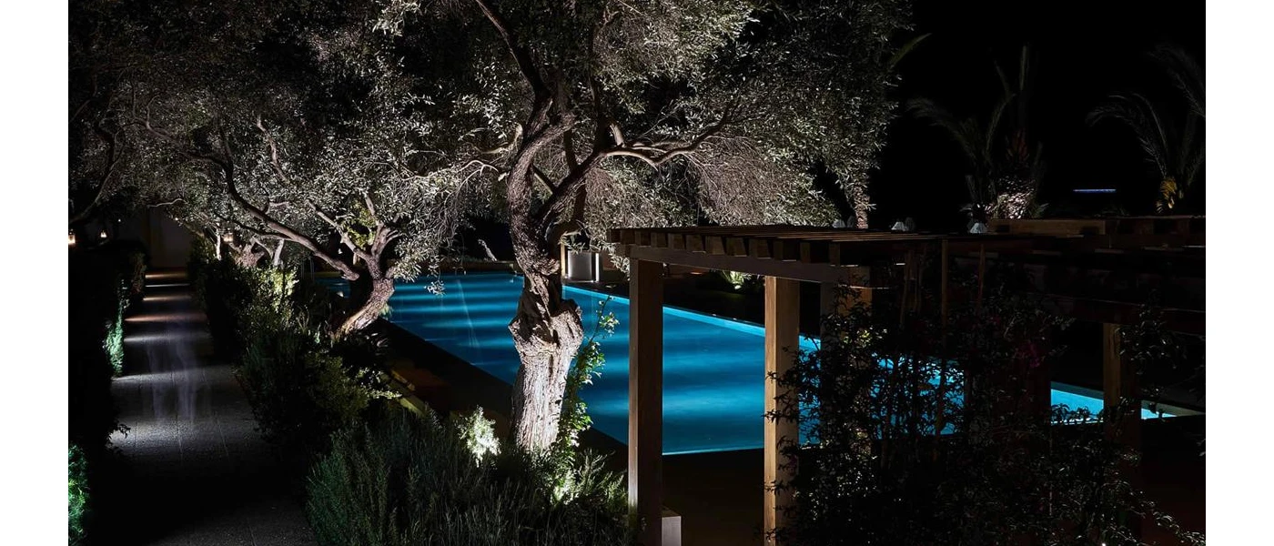 Outdoor swimming pool after dark surrounded by greenery and lit but underwater lighting
