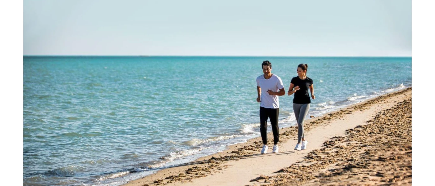 Couple jobs along a golden beach as waves lap at the shore 