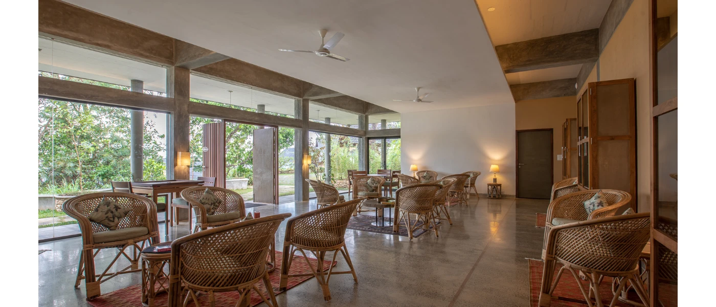 Lounge area with tiled floors and white walls and ceiling, rattan-style chairs and coffee tables and floor-to-ceiling windows