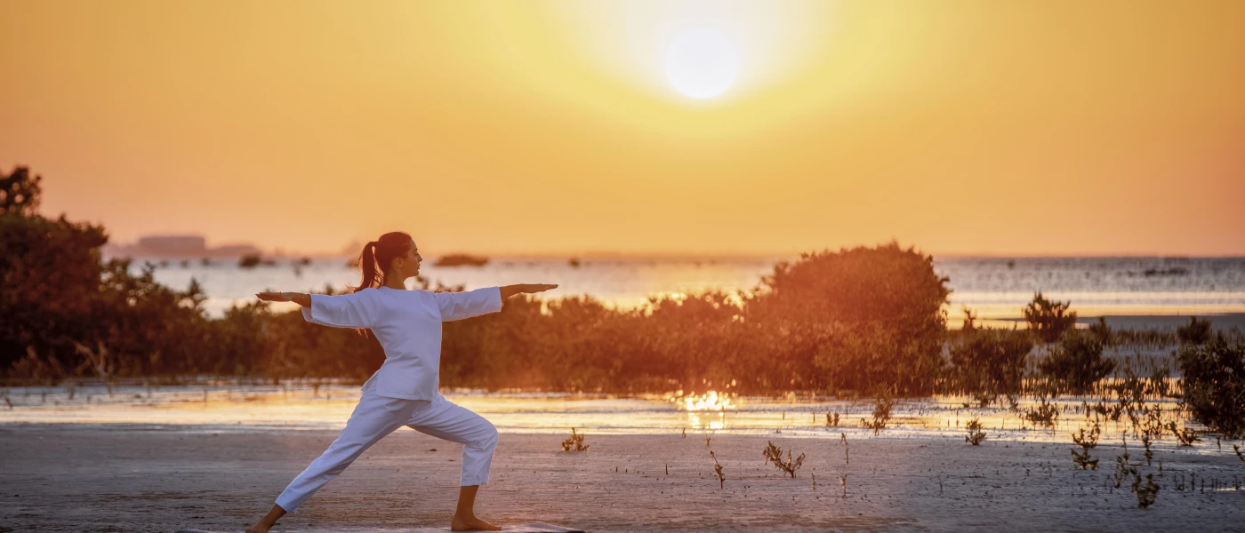 Woman in white practices yoga on the beach as the sun rises or sets