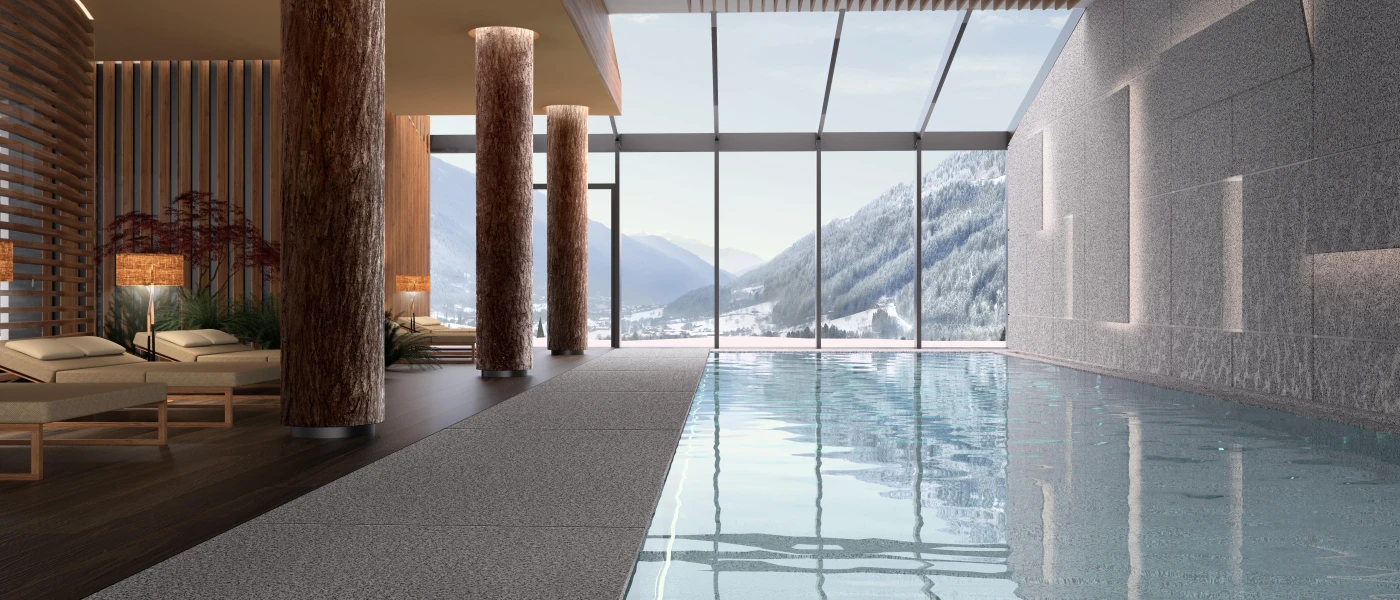 Indoor pool with a glass ceiling and full-length windows, lined with pillars and cushioned loungers