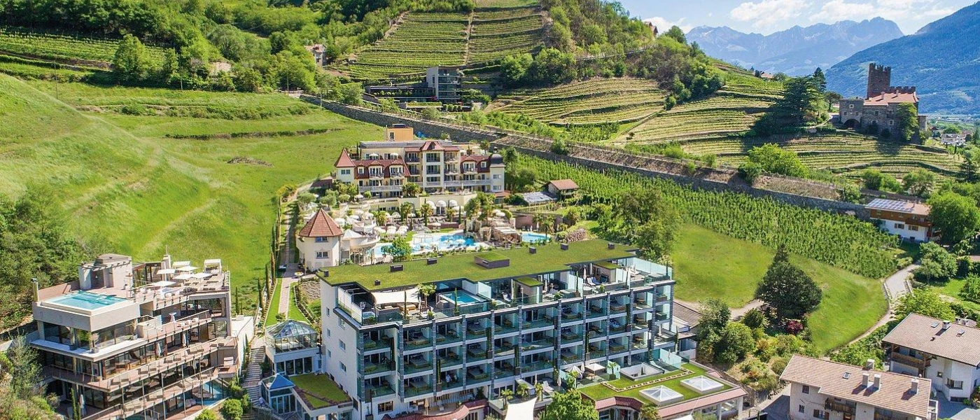 Multi-storey resort among green hills and mountains, with terracotta rooftops, white walls and a central swimming pool surrounded by gardens