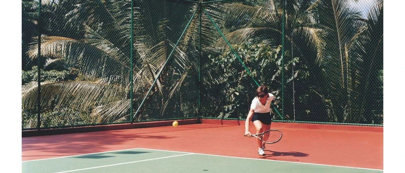 Tennis court with jungle surroundings and a player in sunglasses about to hit the ball