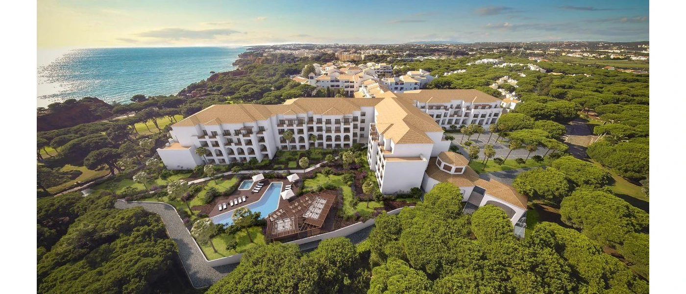 Multi-storey white building on a leafy hillside, peppered with pools and pathways and with an ocean view
