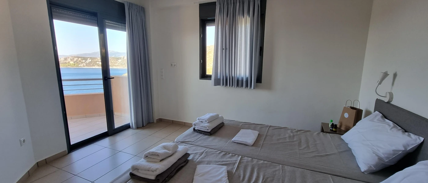 Simple bedroom with twin beds, white walls and a balcony with a sea view