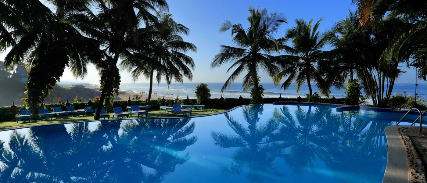 Circular swimming pool edged by palms and with a view of the ocean in the distance