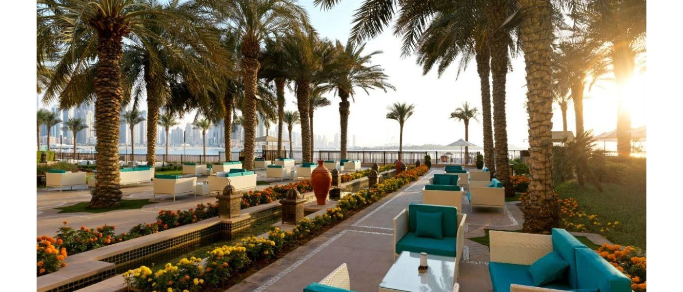 Outdoor sea-facing terrace cloaked in palm trees with rattan furniture and teal blue cushions