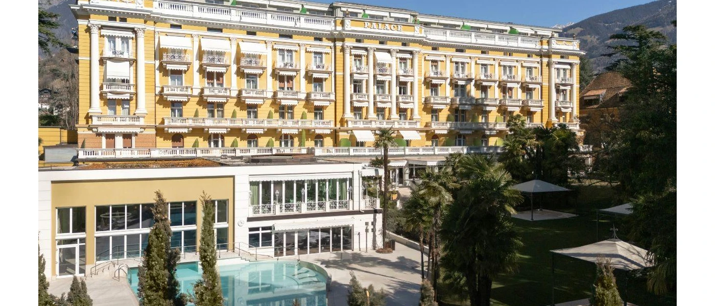 Landscaped gardens, a swimming pool surrounded by palms, and the exterior of Palace Merano