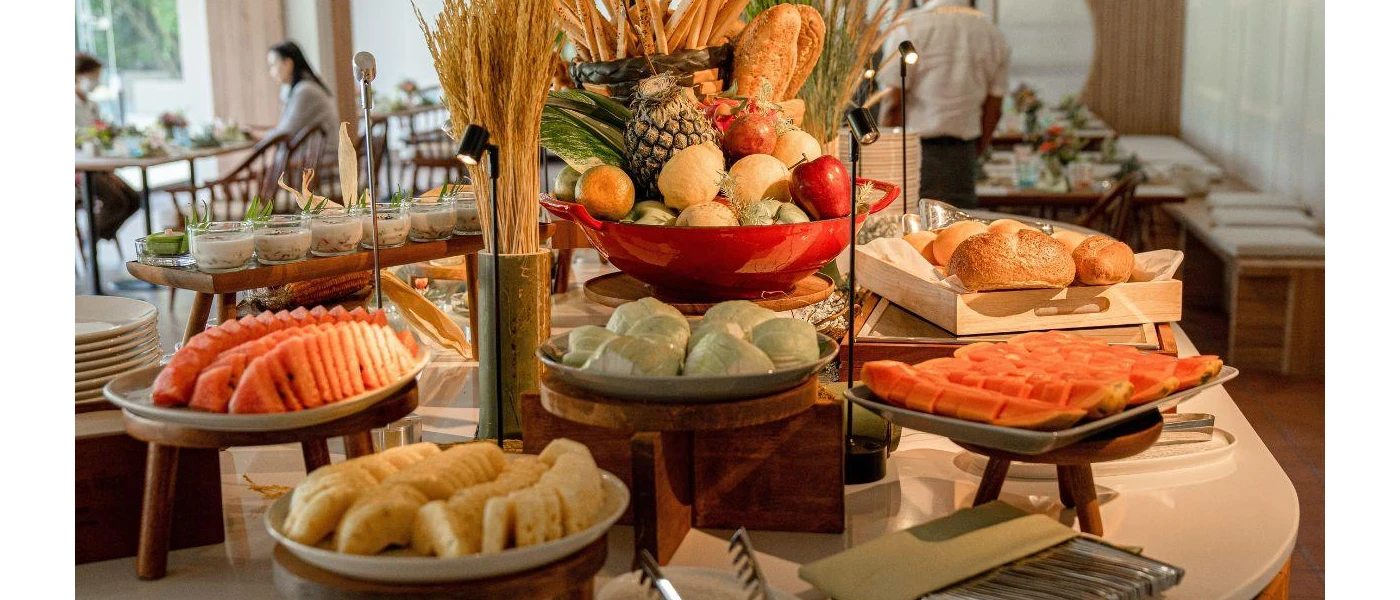 Buffet station with plates of fruit and a tray of bread rolls