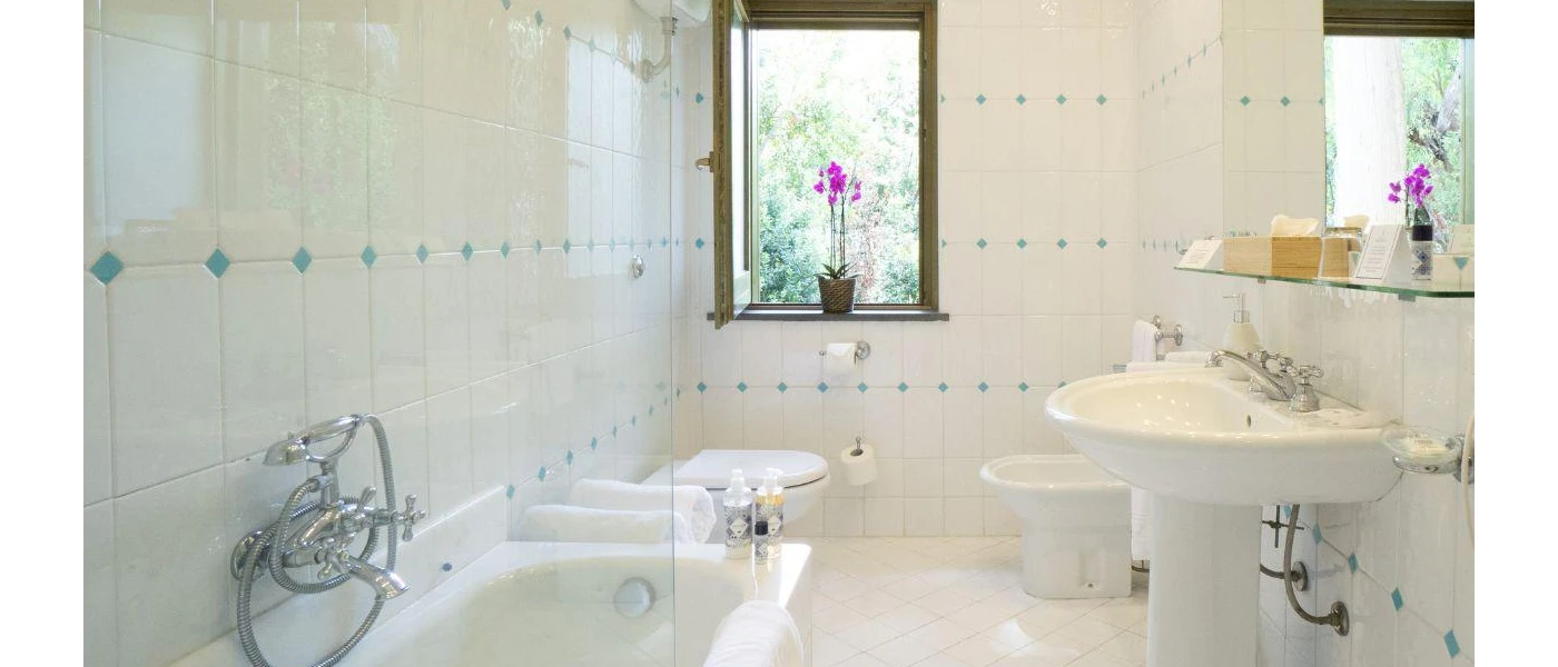 White-tiled bathroom with a potted pink flower in a wooden window frame, a bathtub and sink and mirror