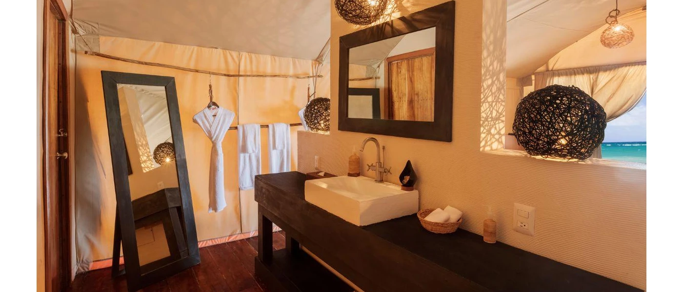 Bathroom with dark-wood mirrors and vanity unit, with a white butler sink and black rattan lanterns and a white robe hanging in the corner