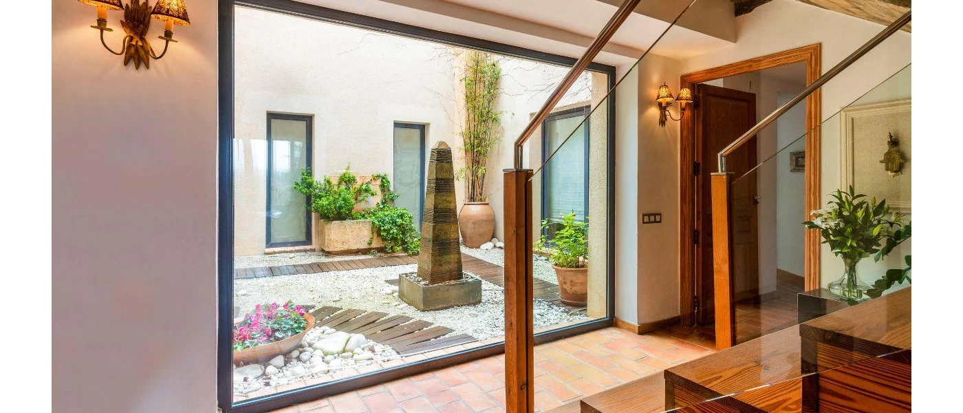 Farmhouse interior with wooden furnishings and a central outdoor courtyard with terracotta plant pots and a stone fountain feature