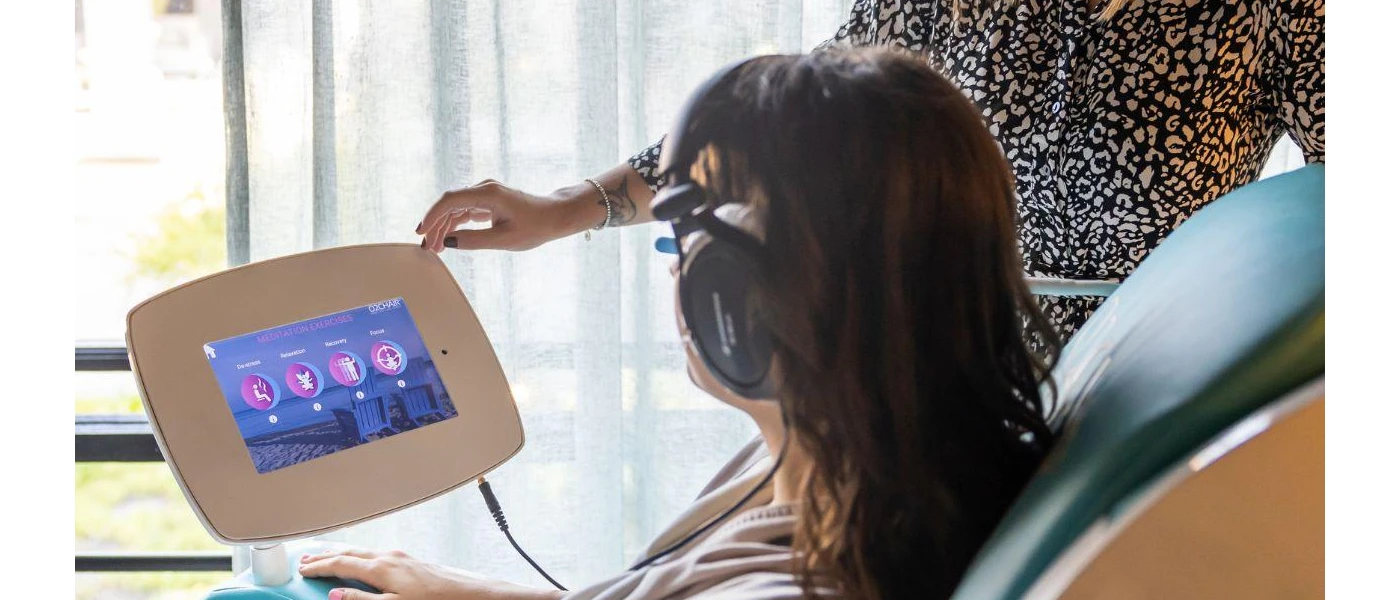 Woman sitting in a chair with a machine, choosing from options that list De-stress, Relaxation, Recovery and Focus