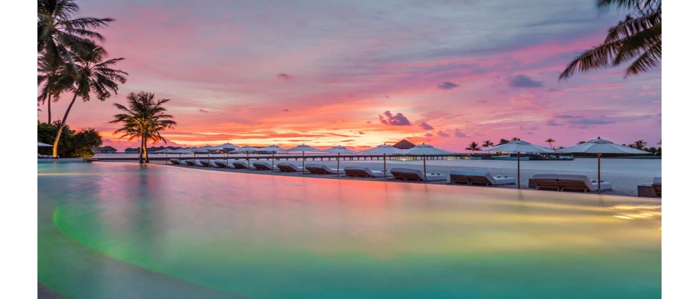 Infinity pool overlooking the beach and palm trees as the sun sets over the Indian Ocean horizon