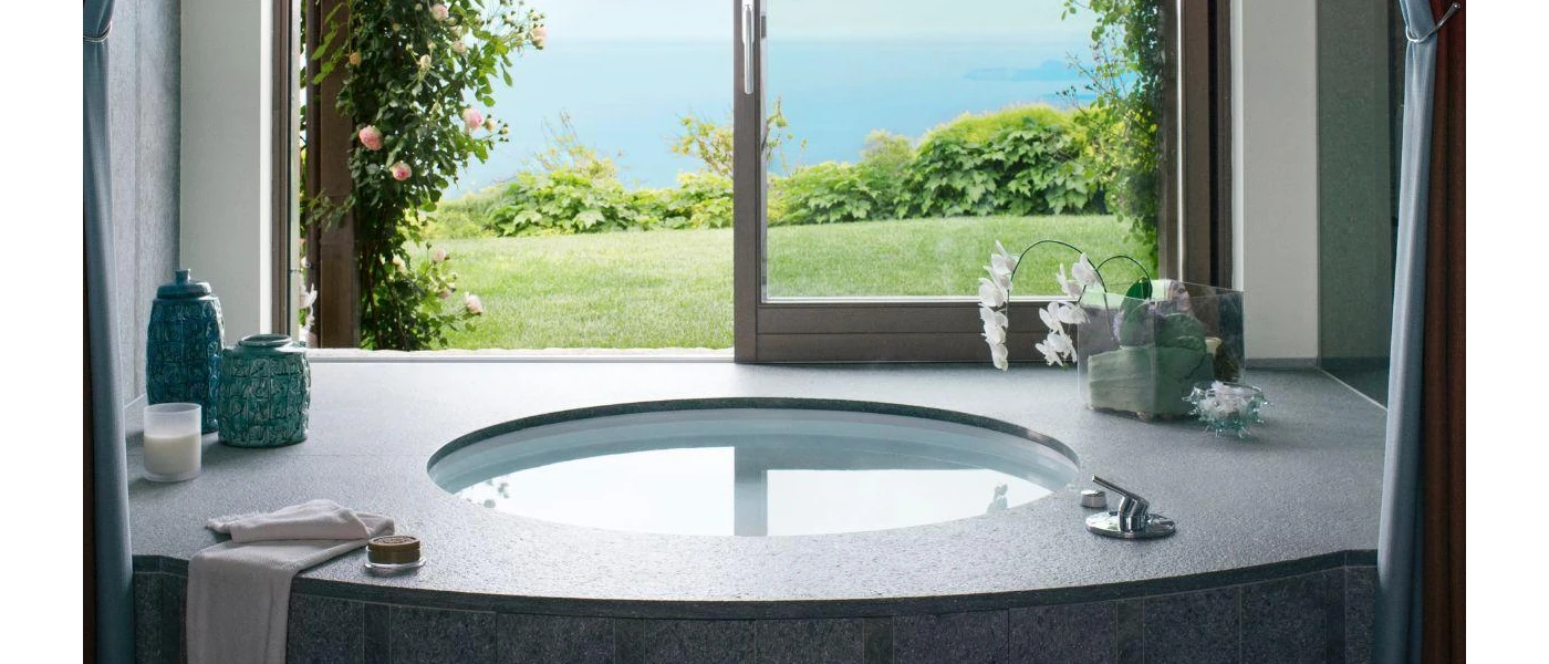 Vanity unit with a round sink and accessories under an open window with a garden and lake view