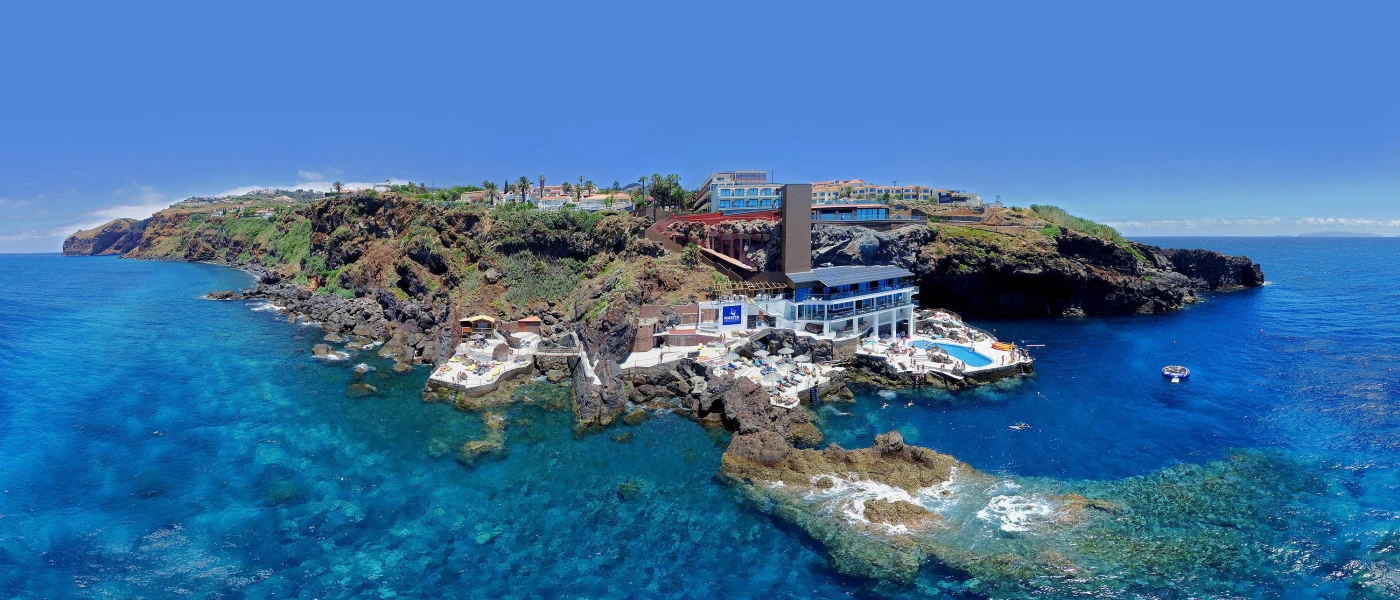 View of Sentido Galasol from the ocean, a white resort surrounded by rocky cliffs with direct access to the ocean