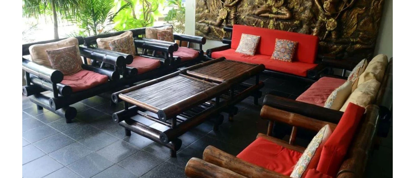 Seating area with dark-wood chairs and coffee table, red cushions and an intricate wall mural depicting Hindu gods