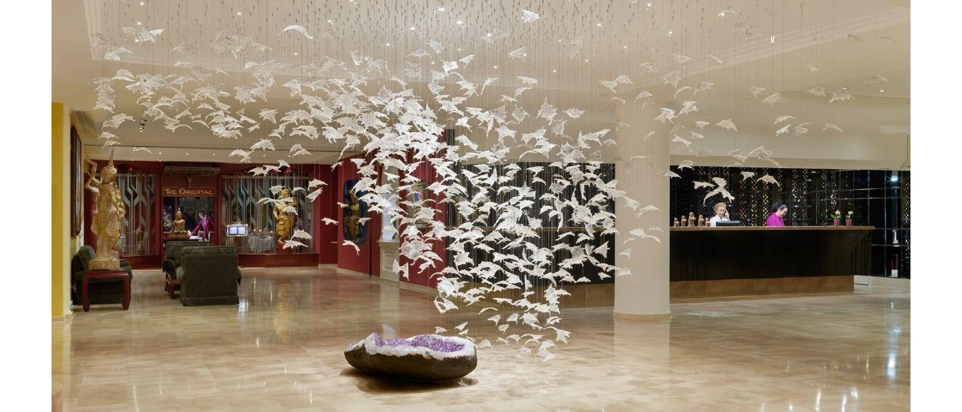 Modern art mural, with a sculpture of an open crystal on the floor, topped with hundreds of white cut outs designed to look like birds suspended from the ceiling