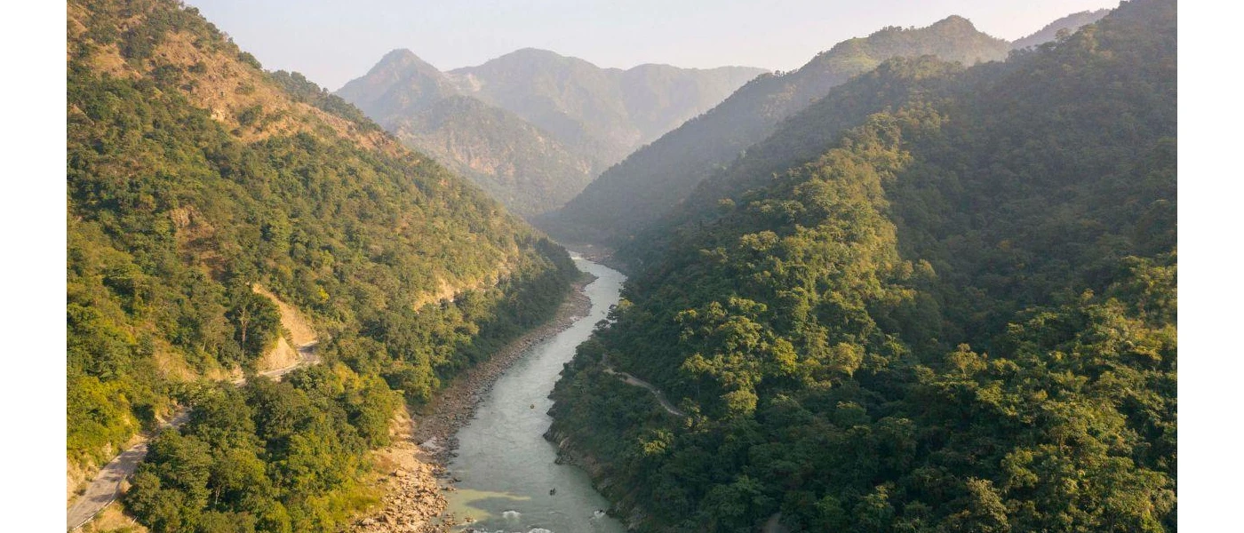 A curvy river runs along green-cloaked peaks under a misty blue sky
