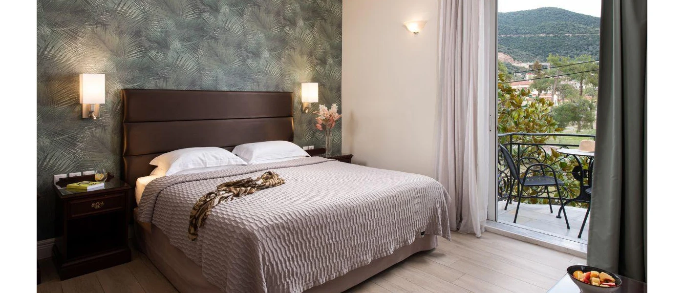 Hotel room with a dark wall, brown padded headboard, white bedding and neutral cushions and balcony with furniture