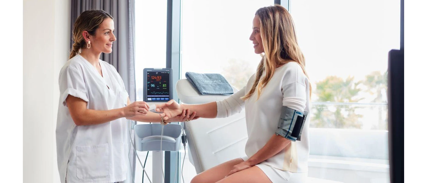 Woman in white sits in a bright room hooked to a machine as a specialist checks her readings 